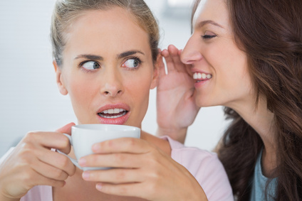 Smiling woman telling secret to her friend while drinking coffee